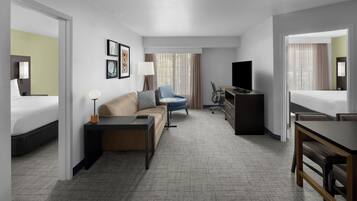 Habitación de hotel con cama, sofá, escritorio, silla, televisión y ventana con cortinas.