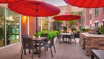 Un espace extérieur aménagé en terrasse, avec des tables et des chaises, des parasols rouges et une cheminée en pierre.