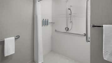 Un área de ducha moderna con puerta de cristal, barra de apoyo y perchero.