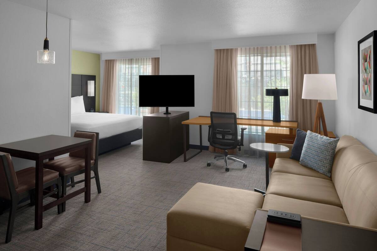 Una habitación de hotel con una cama, un escritorio con computadora, un sofá y un televisor.