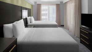 A modern hotel room with two beds, a flat-screen TV, and a large window with sheer curtains.