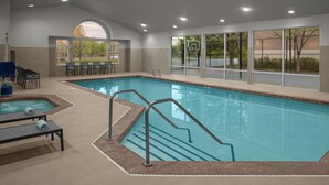An indoor swimming pool with clear glass walls, a separate lounge area with chairs, and a basketball hoop visible through the windows.