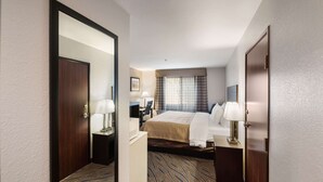 A hotel room with a large bed, a desk with a chair, a mirror, and a window with curtains. - Quality Inn Midvale - Salt Lake City South (Midvale)