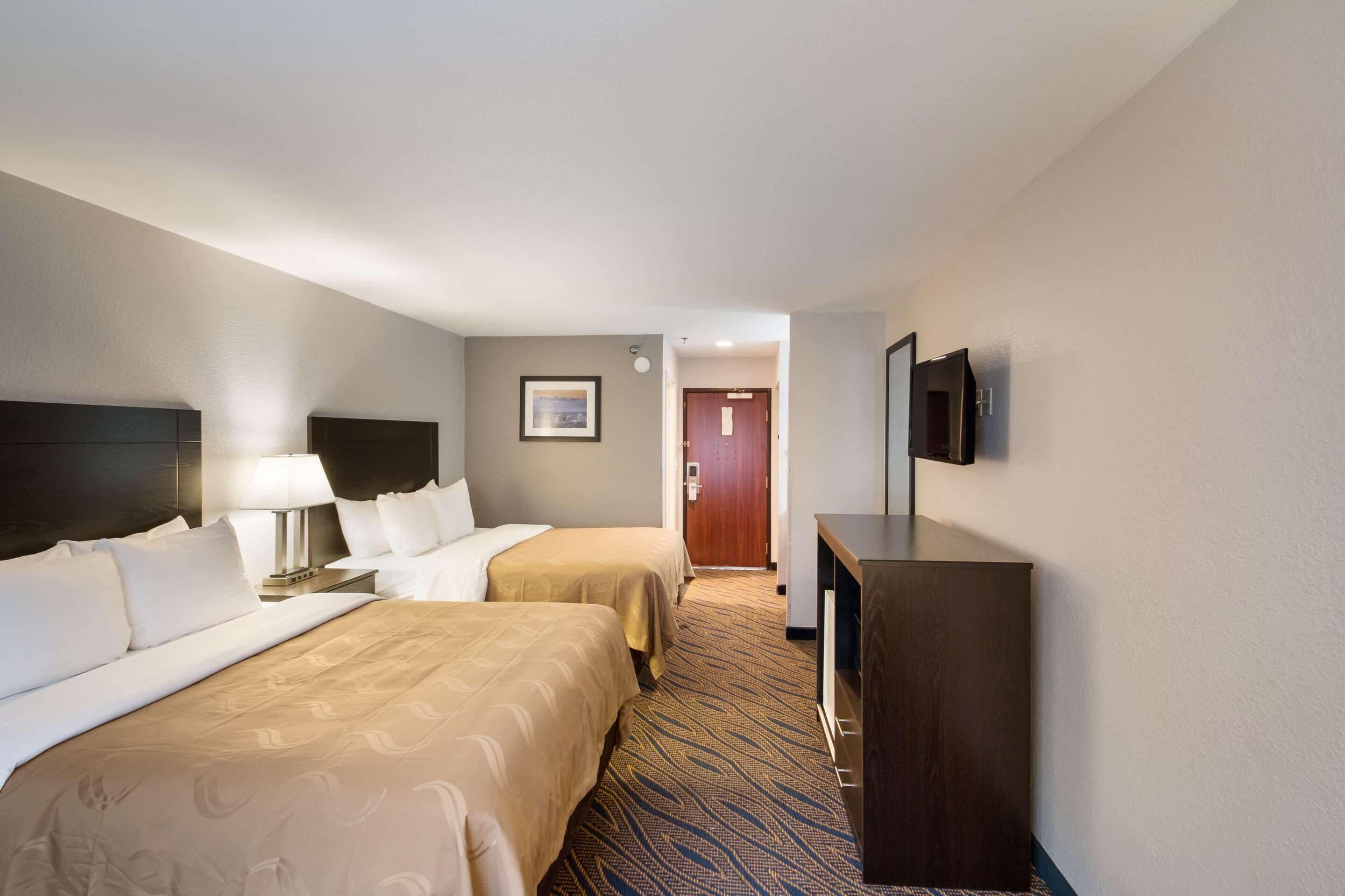 A hotel room with two beds, a desk, a television, and a door leading to another room.