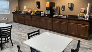 A modern kitchen with a long counter, built-in appliances, and a seating area with tables and chairs. - Quality Inn Midvale - Salt Lake City South (Midvale)