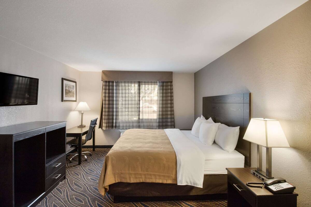 Ein Hotelzimmer mit Bett, Schreibtisch, Stuhl, Fernseher und Telefon.