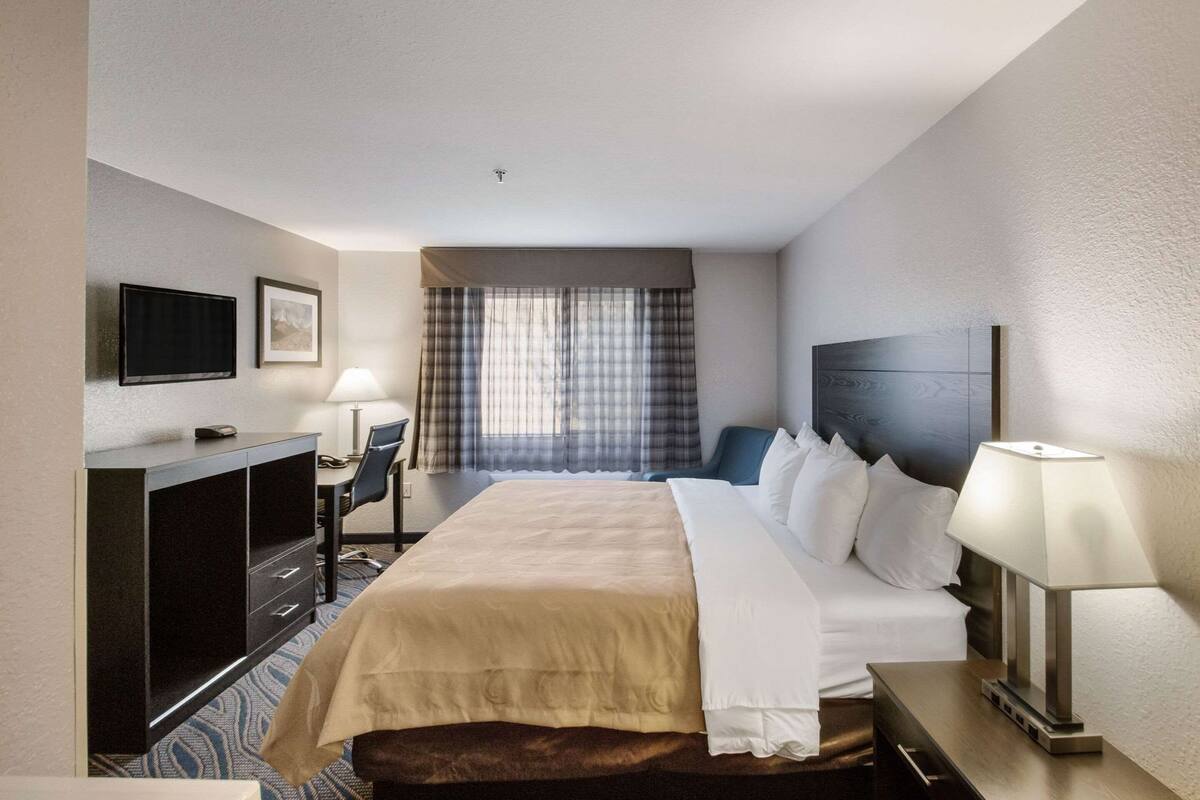 Ein Hotelzimmer mit Bett, Schreibtisch, Stuhl, Fernseher und Vorhängen.