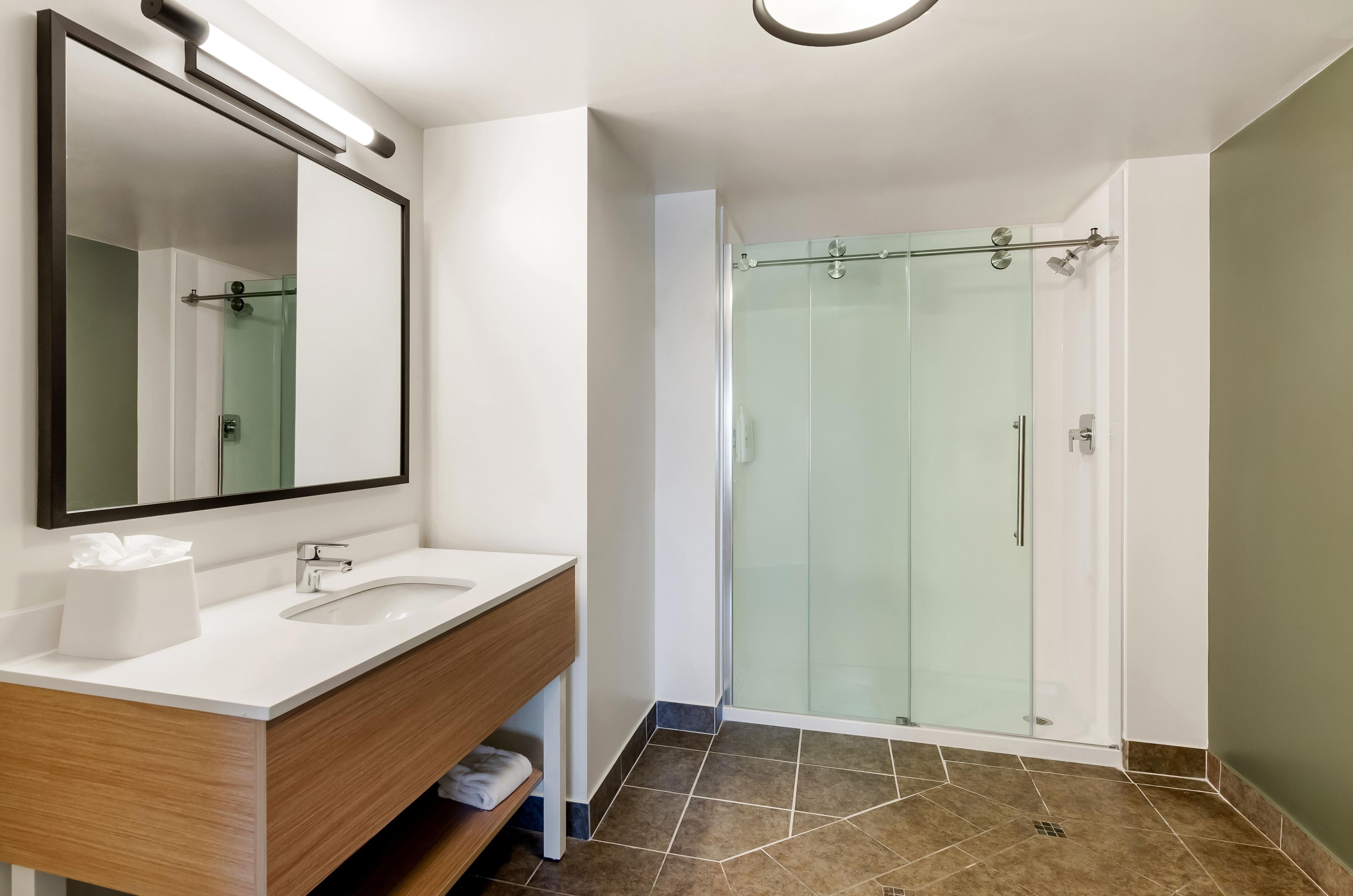 A modern bathroom with a glass-enclosed shower, a large mirror, and a wooden vanity.