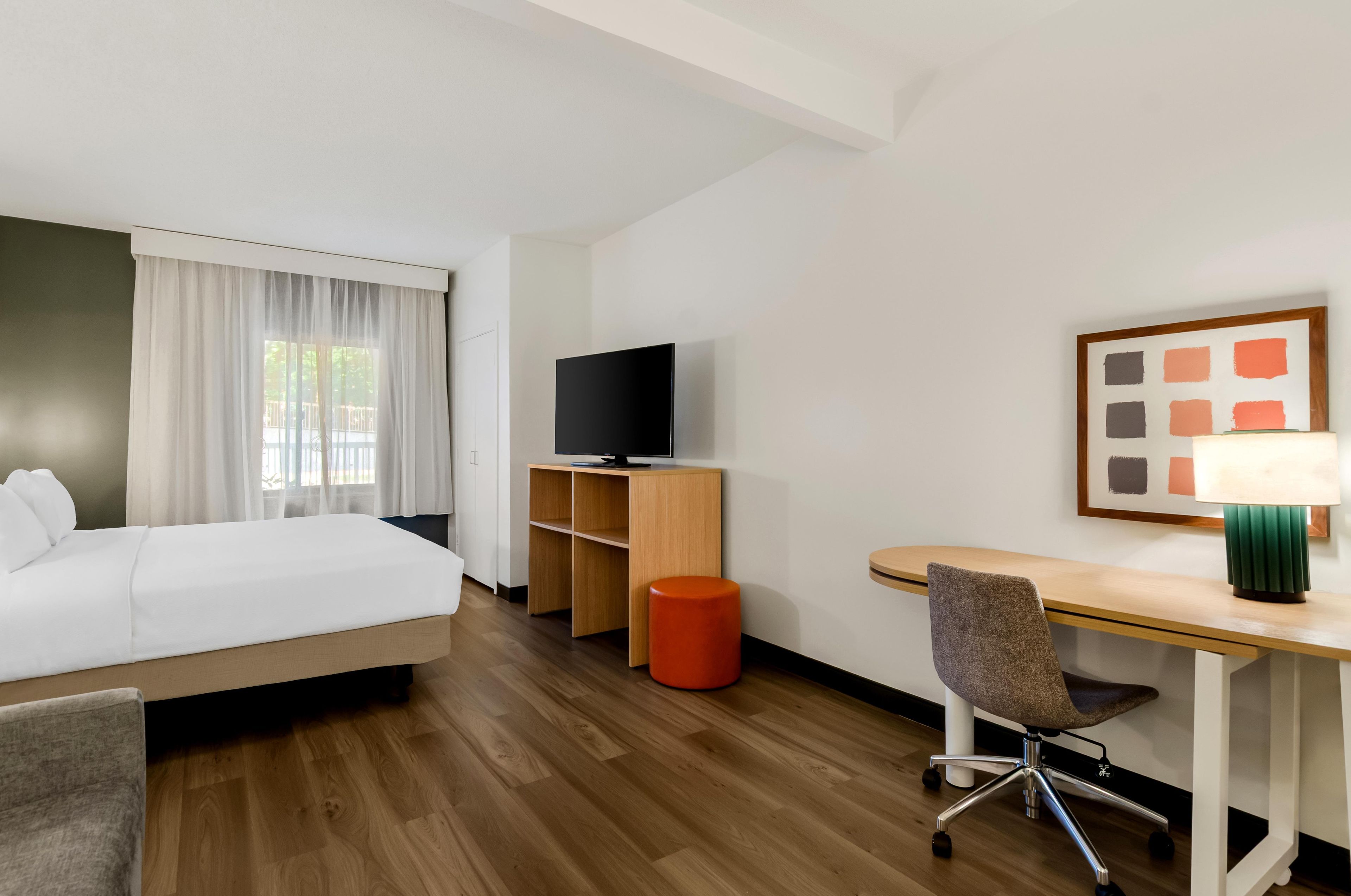 A hotel room with a bed, a desk, a chair, a television, and a window with curtains.