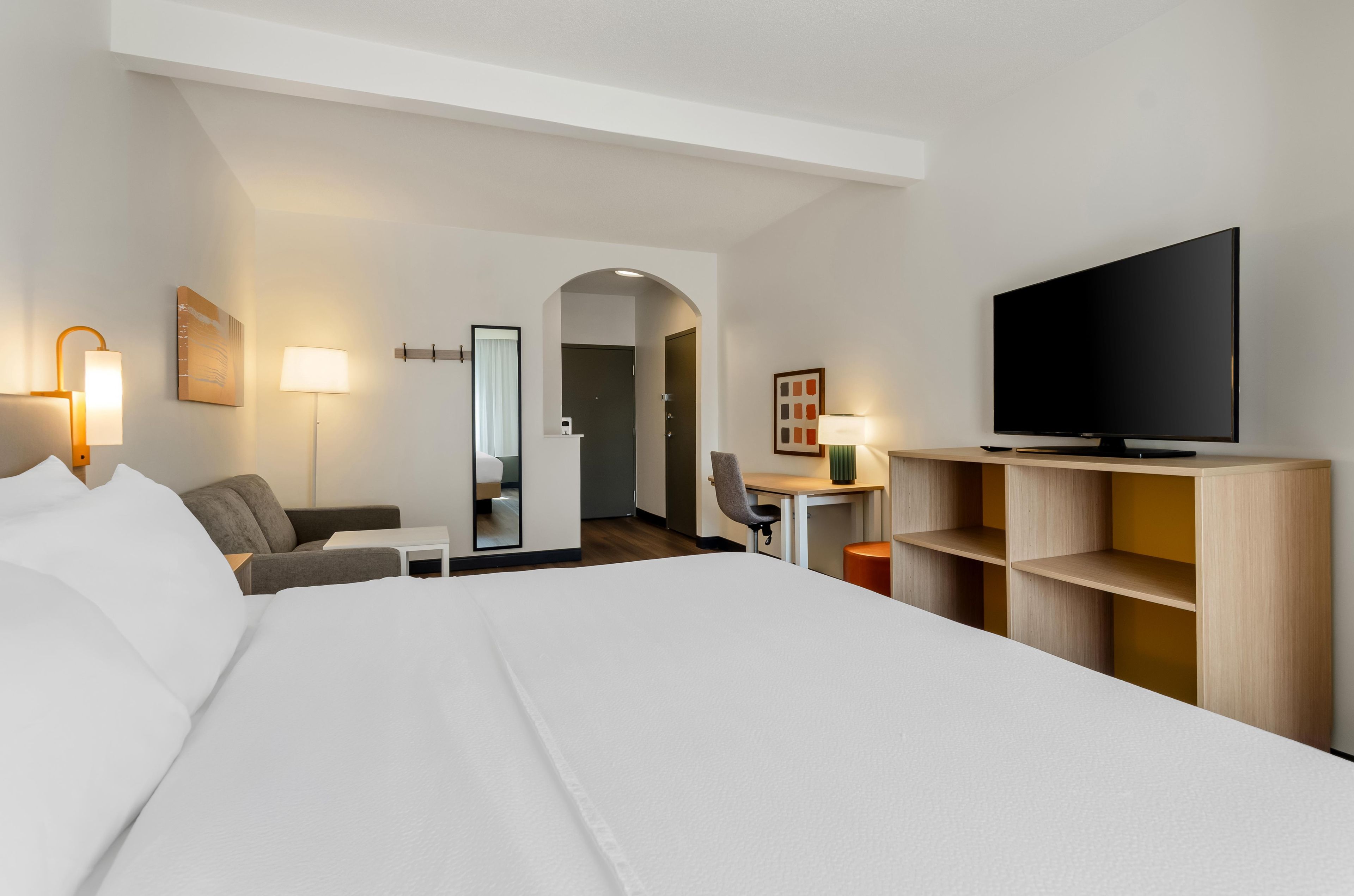 Una habitación de hotel con una cama grande, un escritorio, una silla, un televisor y un espejo.