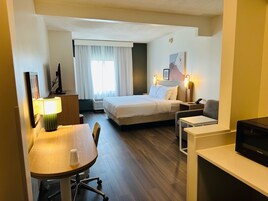 Habitación de hotel con cama, escritorio, silla, televisor y ventana con cortinas.
