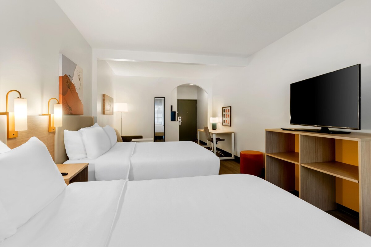 Una camera d'albergo con due letti, una TV, una scrivania e una sedia.