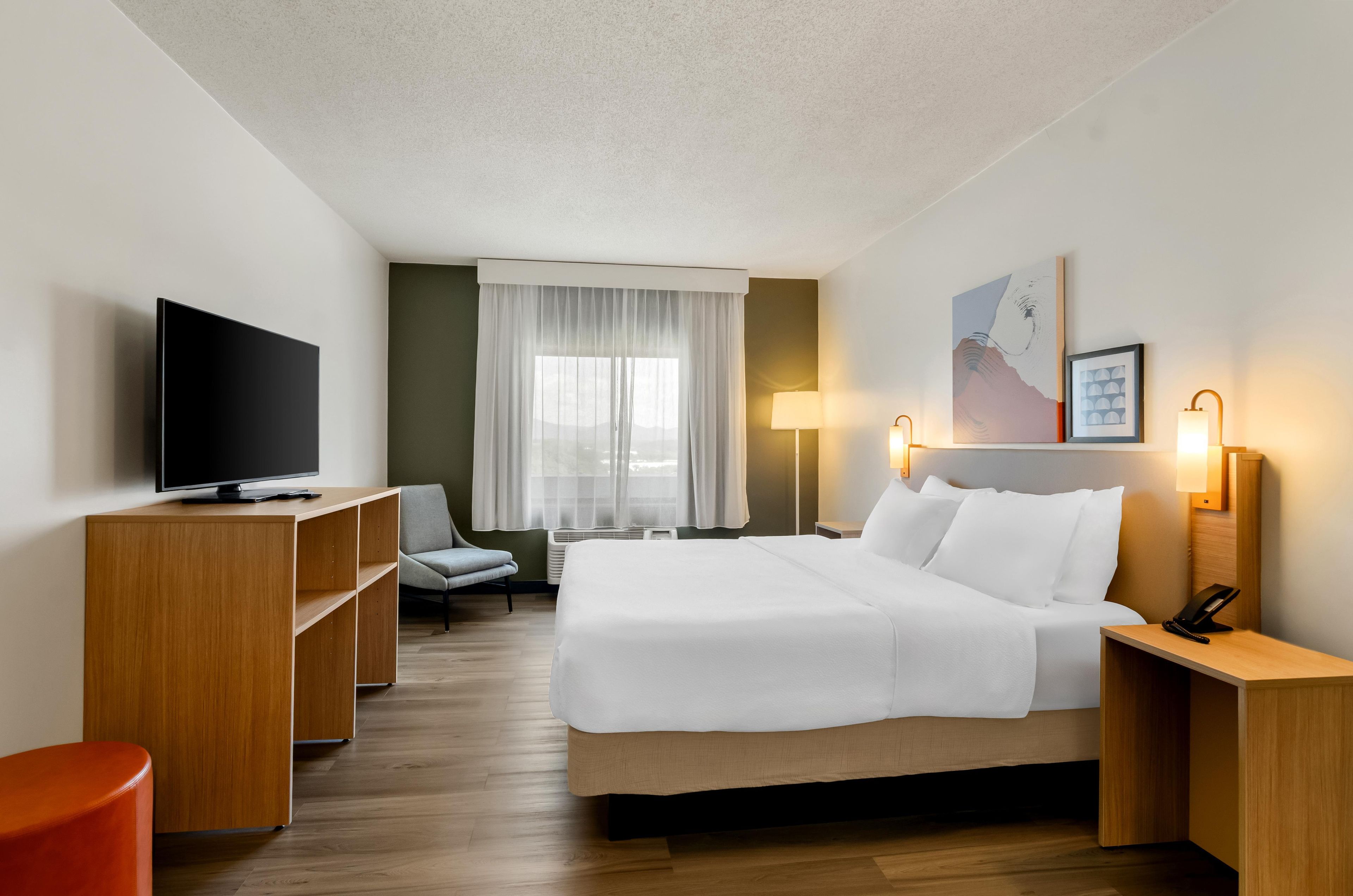 A hotel room with a bed, a TV, a desk, a chair, and a lamp.