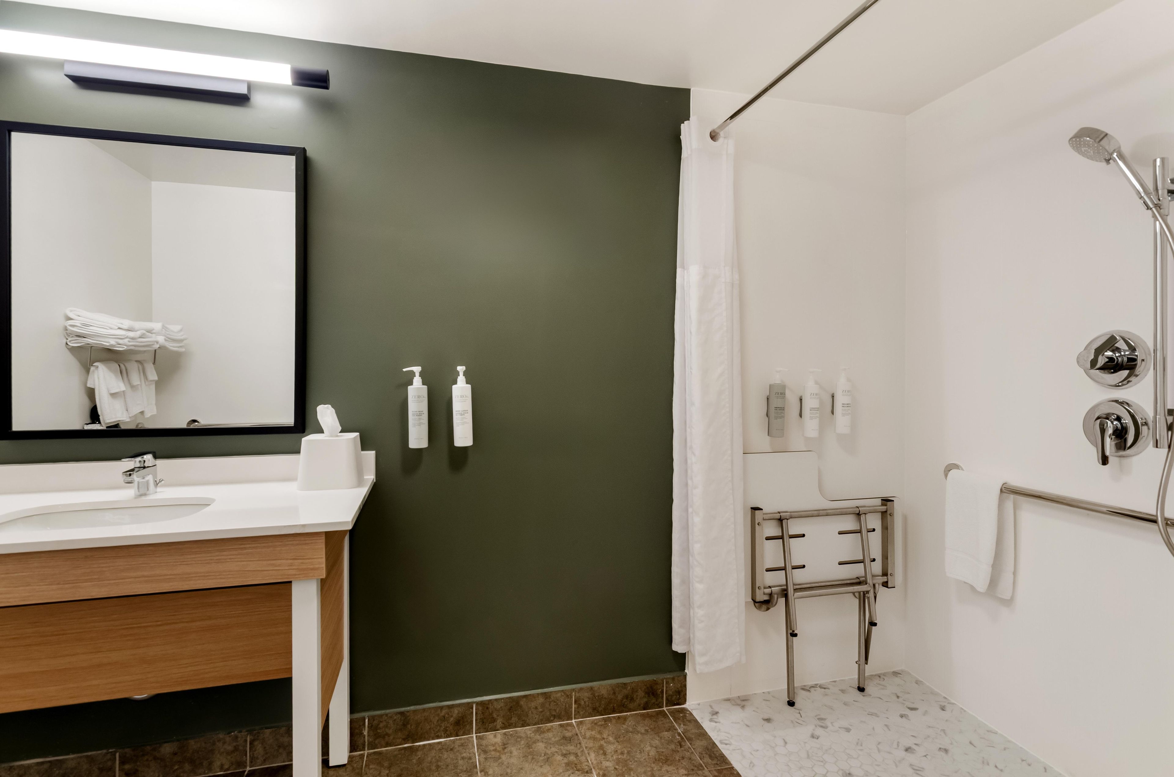 A modern bathroom with a white sink, a mirror, a towel rack, and a shower area.