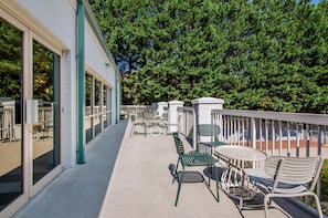 A covered outdoor patio with tables and chairs, a railing, and a view of trees. - Spark by Hilton Salem East Electric Road (Salem)