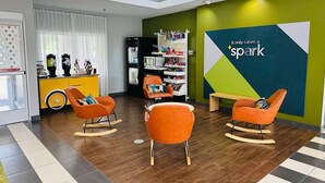 A modern lobby with a green accent wall, a seating area with orange chairs, a refrigerator, and a vending machine. - Spark by Hilton Salem East Electric Road (Salem)
