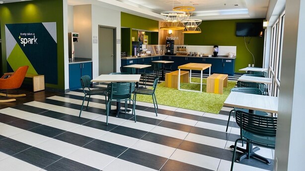 A modern café with a striped floor, green walls, and a central seating area with tables and chairs. - Spark by Hilton Salem East Electric Road (Salem)