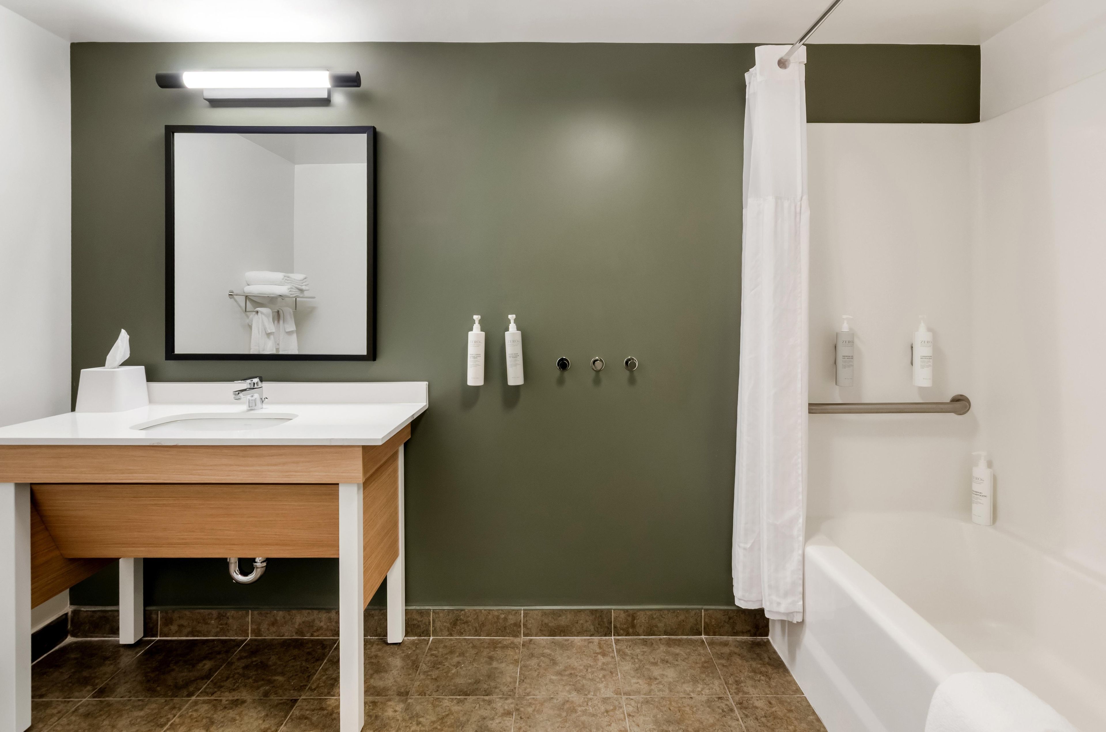 Un baño con tocador de madera, un espejo, toallero y cortina de ducha.