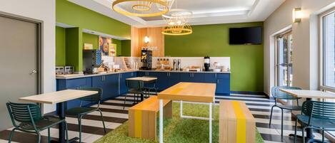 Un café moderno con piso a cuadros, paredes azules y verdes, y un área central de asientos con mesas y sillas.