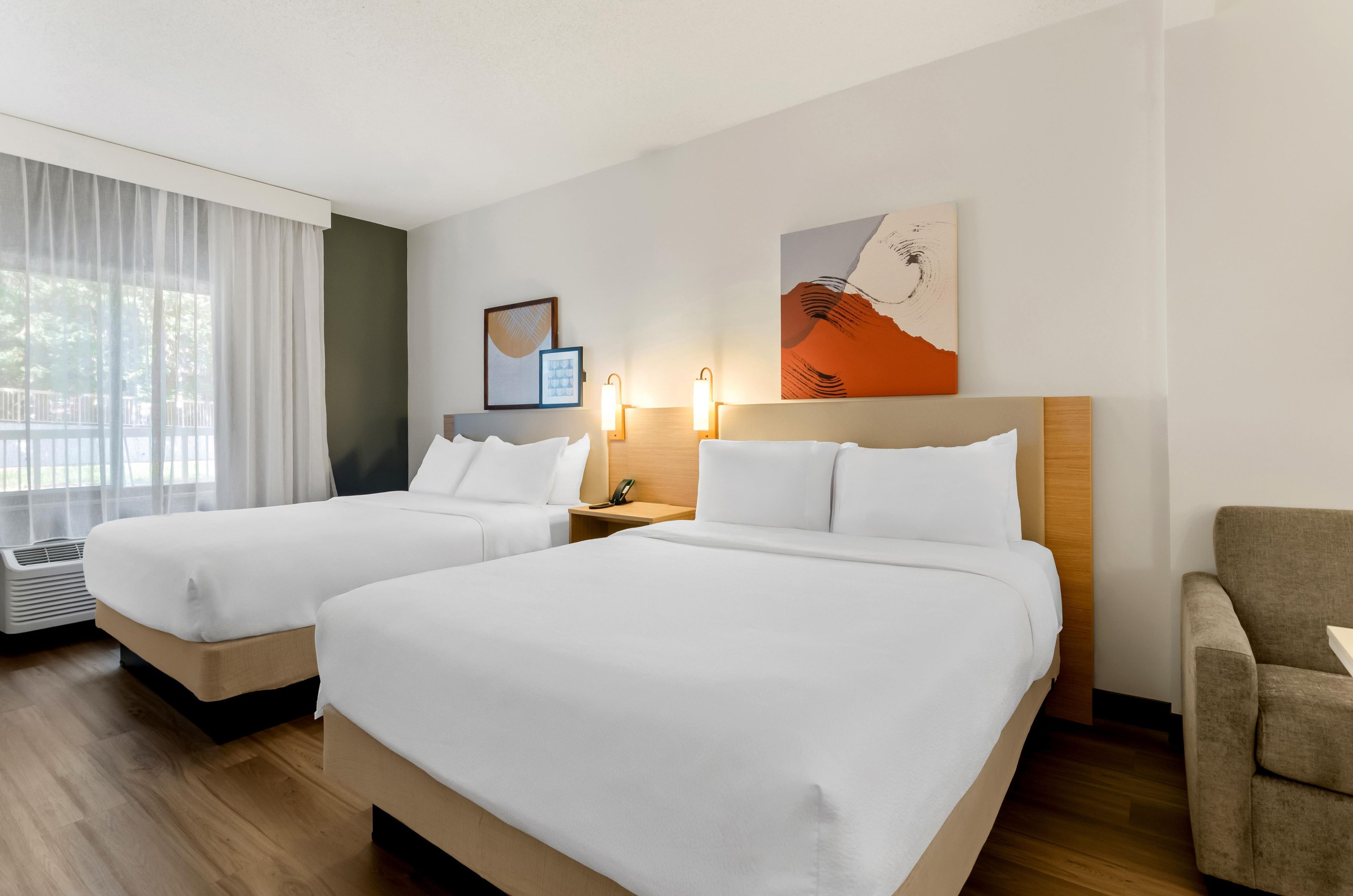 A hotel room with two beds, a desk, a chair, and artwork on the wall.