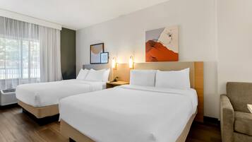 A hotel room with two beds, a desk, a chair, and artwork on the wall.