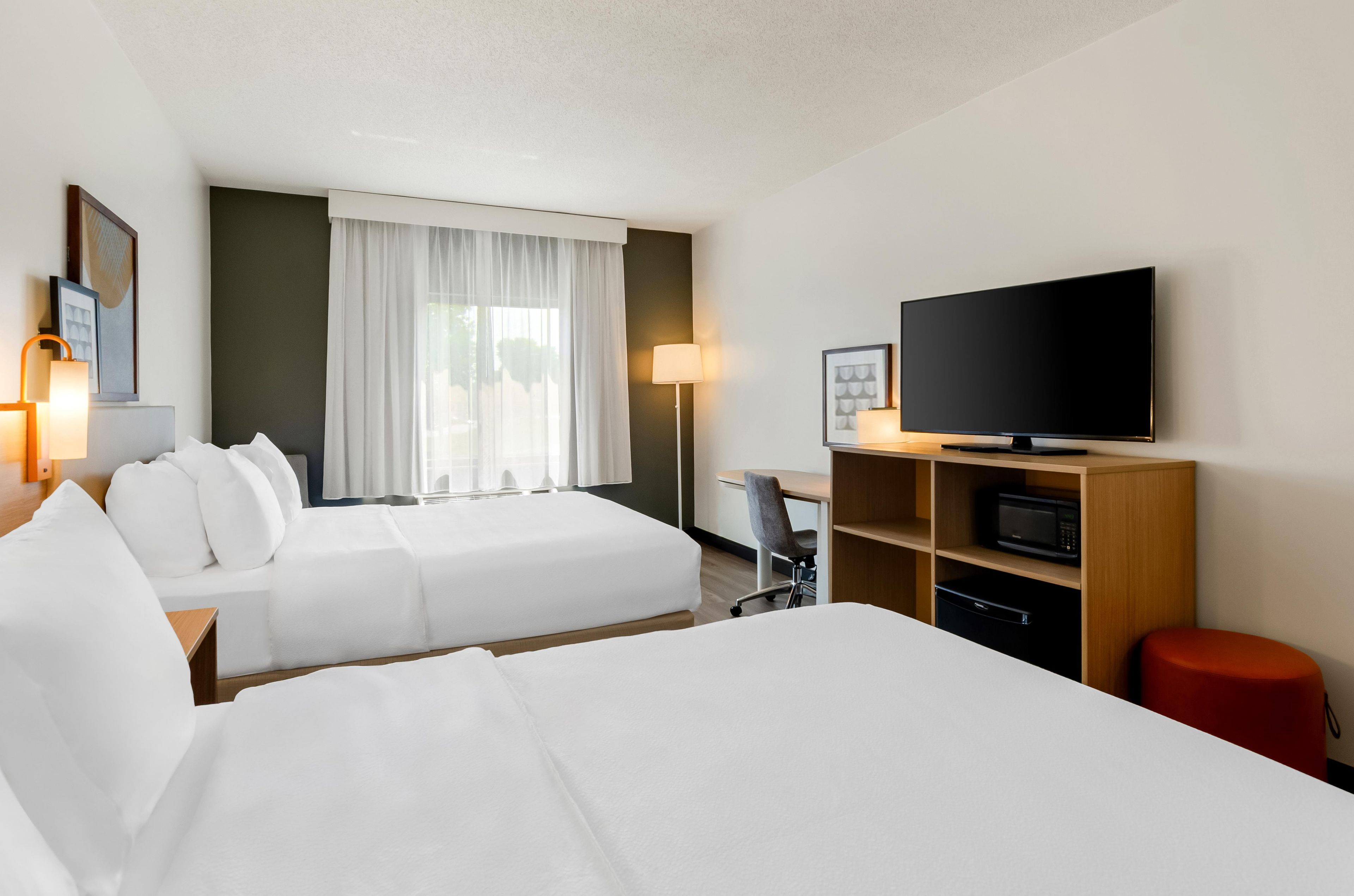 A hotel room with two beds, a television, a desk with a chair, and a microwave.