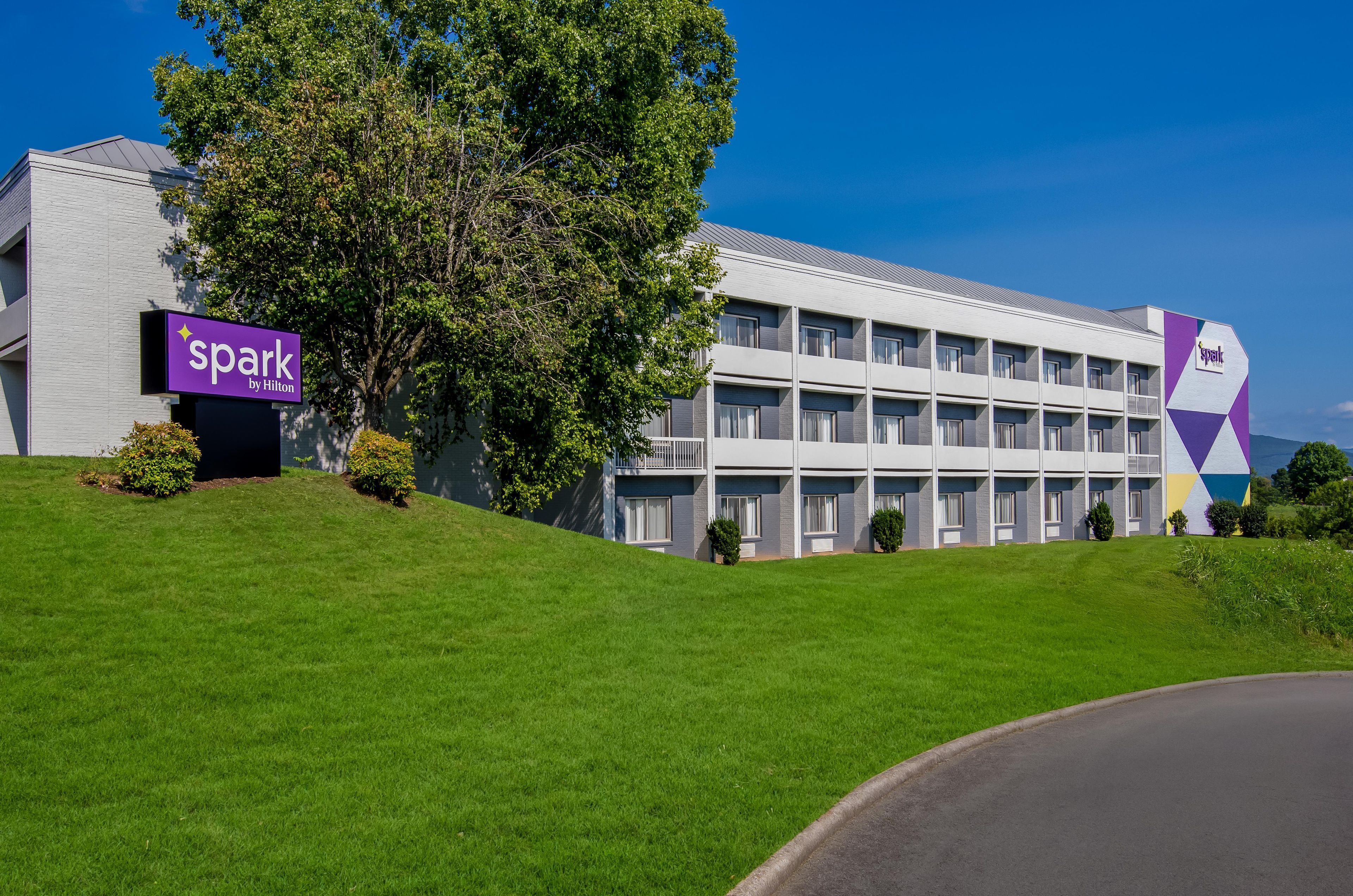 A modern hotel building with a sign reading 'spark by Hilton' and a large tree in front.