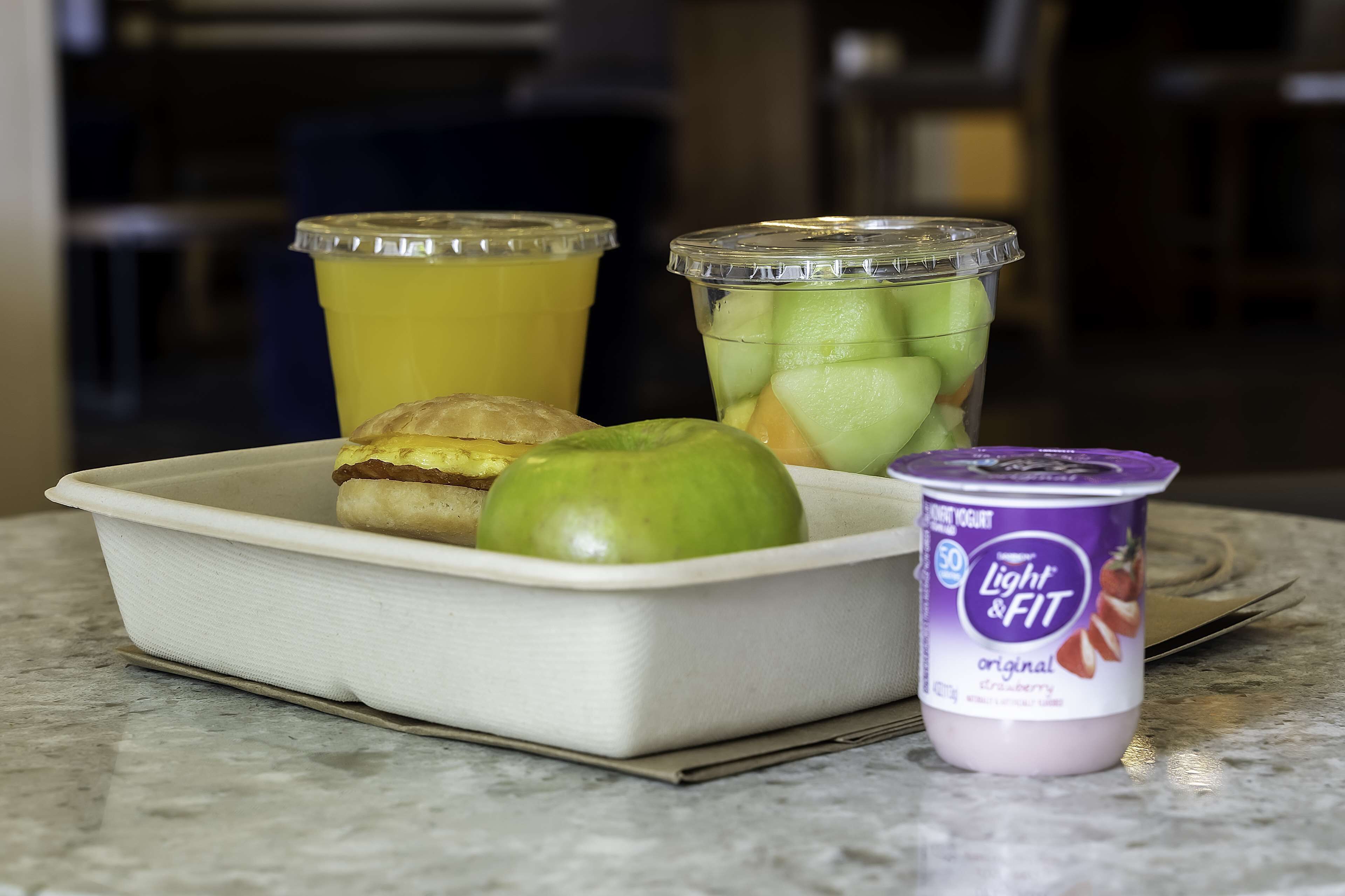 Bandeja de comida con un pastel, una manzana verde, un envase de yogurt Light & Fit y un envase de jugo de frutas.