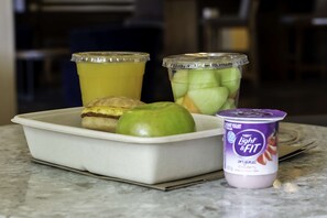 A meal tray with a pastry, a green apple, a container of Light & Fit yogurt, and a container of fruit juice.