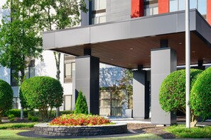 A modern building with a covered entrance, neatly trimmed hedges, and a landscaped garden area.