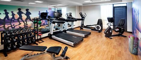 Une salle de sport équipée de tapis de course, de vélos elliptiques, de poids libres et d’un banc de musculation.