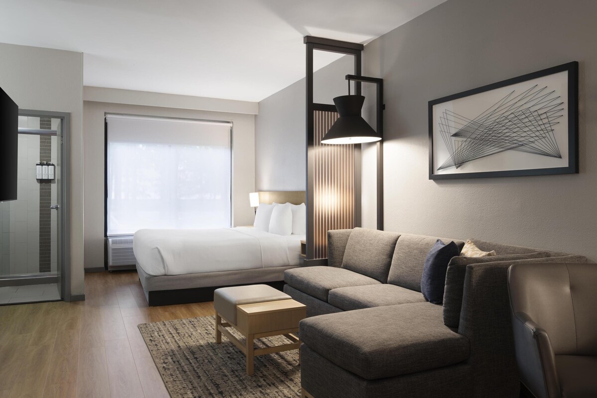 Une chambre d’hôtel moderne équipée d’un lit, d’un canapé, d’un bureau et d’une grande fenêtre.