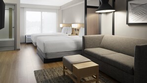 Une chambre d’hôtel moderne avec deux lits, un canapé, une petite table en bois et une grande fenêtre.