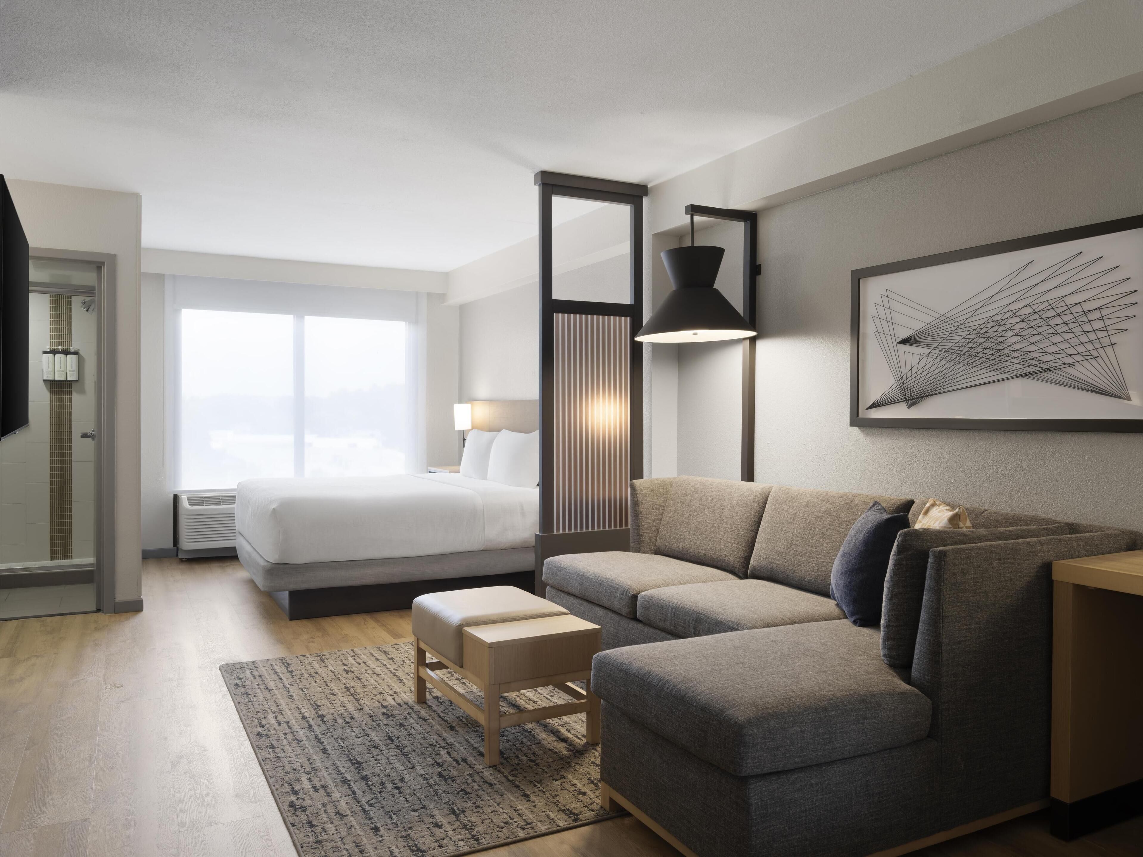Une chambre d’hôtel moderne avec un grand lit, un canapé, une petite table et une grande fenêtre.