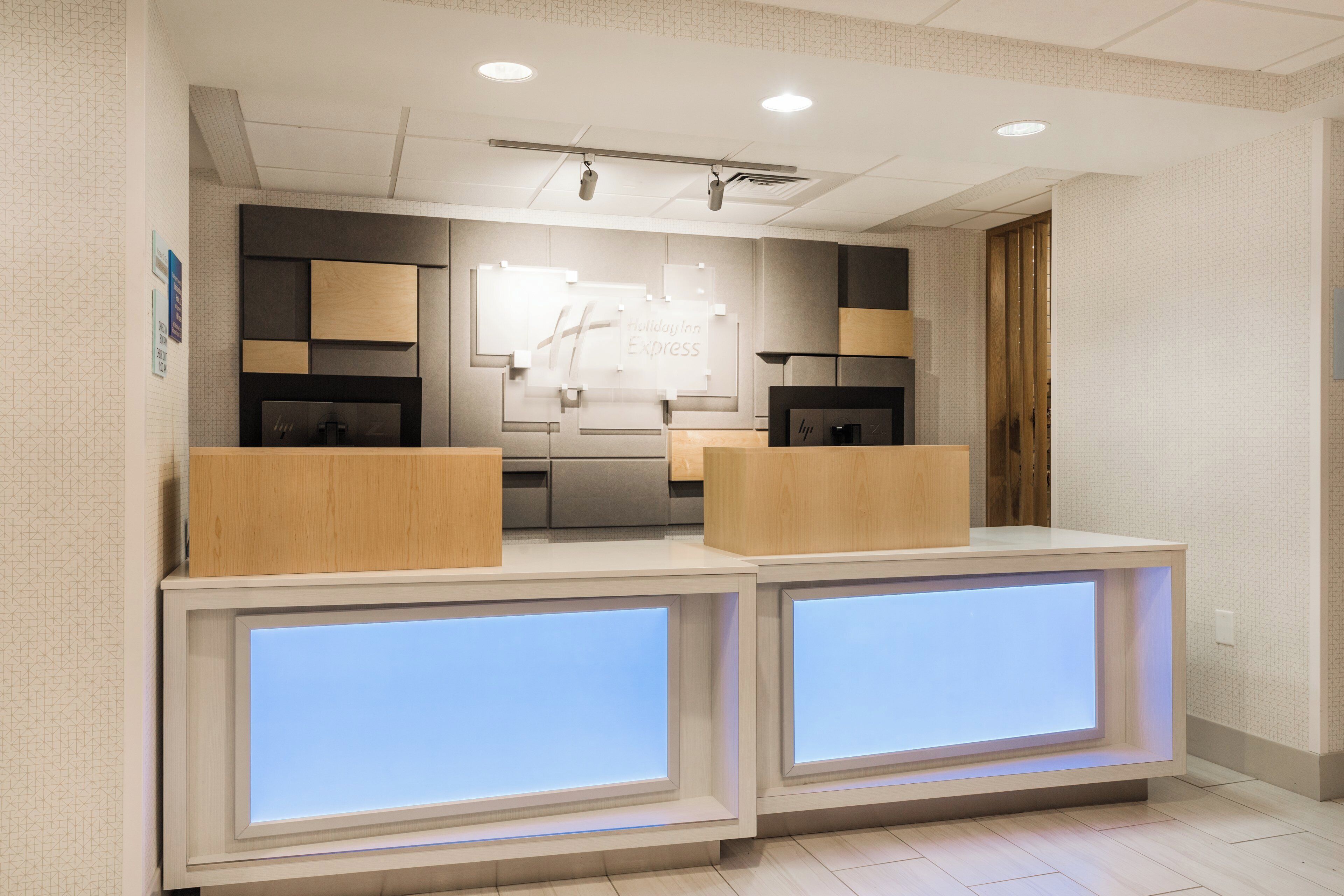 Un espace d’accueil au design moderne, comprenant un comptoir d’accueil doté de panneaux rétroéclairés, un écran mural et un projecteur fixé au plafond.