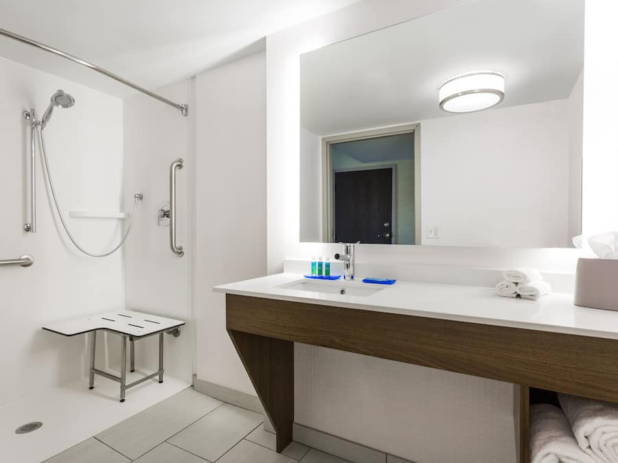 Un baño moderno con ducha, un lavabo con espejo y un perchero para toallas.