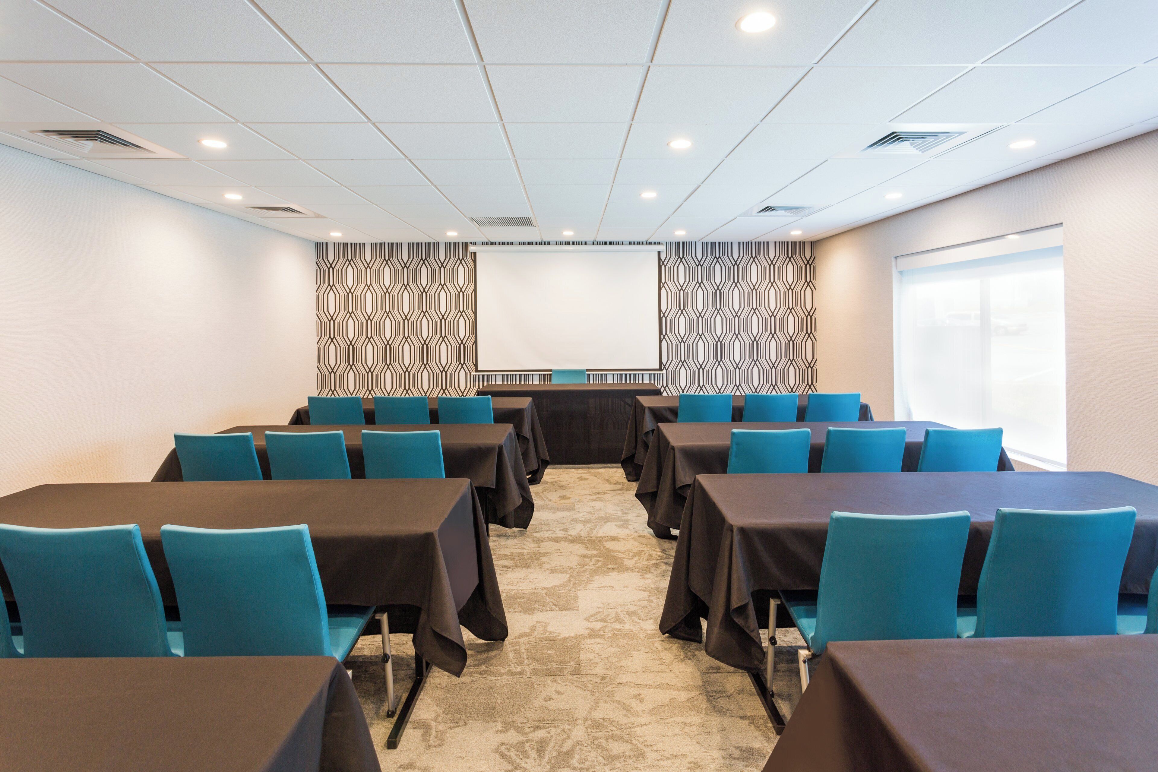 Un salón de conferencias con filas de mesas y sillas, un papel tapiz decorativo y suelo alfombrado.