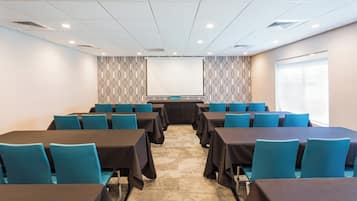 Un salón de conferencias con filas de mesas y sillas, un papel tapiz decorativo y suelo alfombrado.