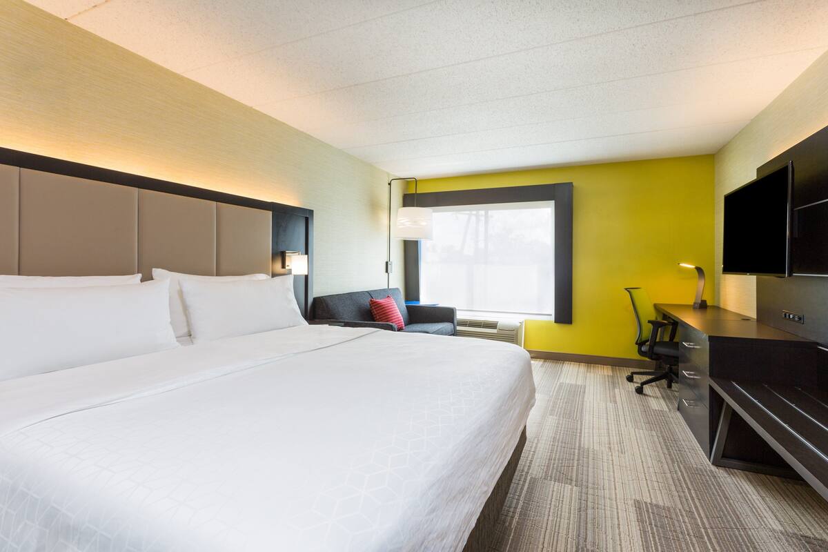 A hotel room with a large bed, a desk, a chair, a TV, and a window with a view.