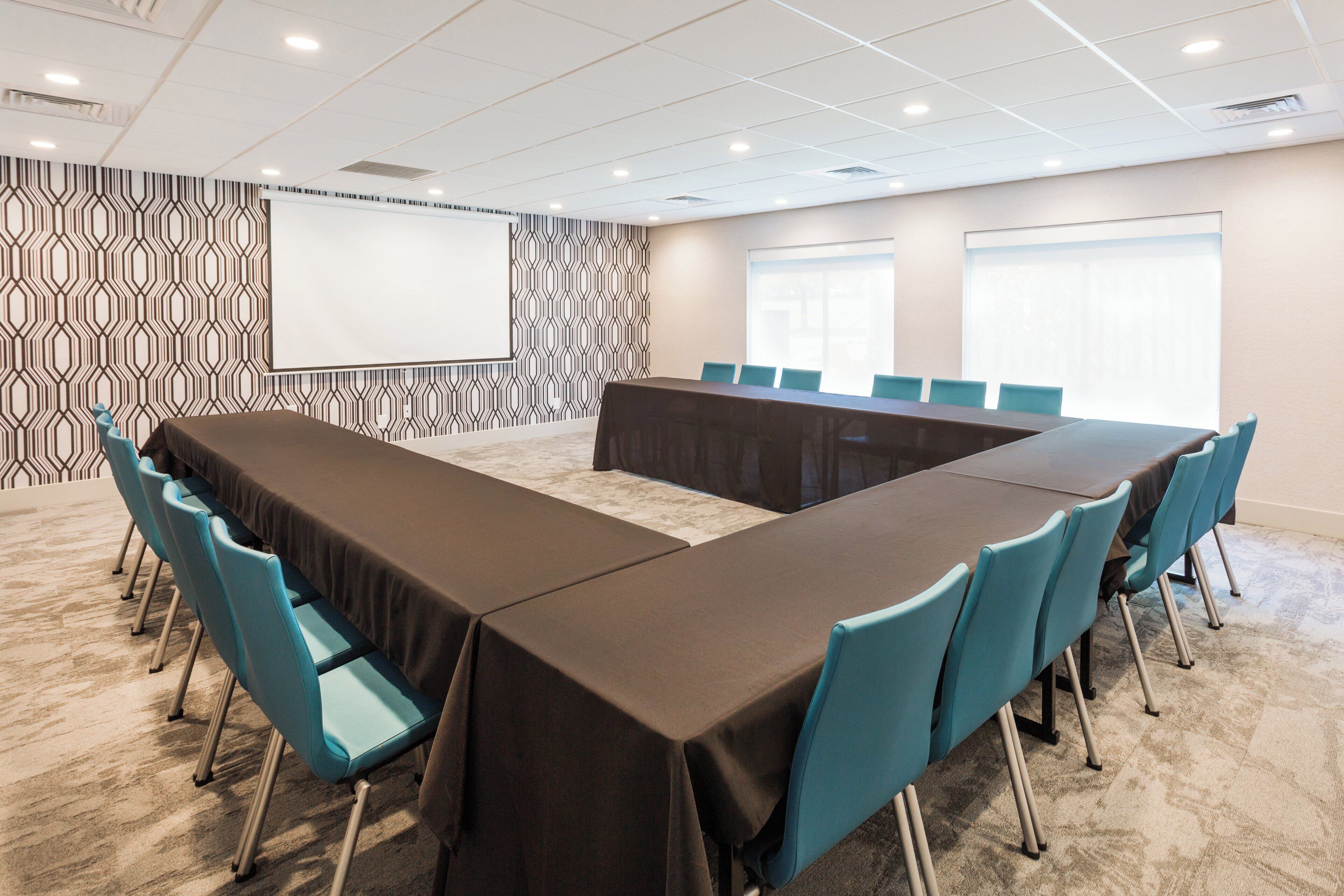 A conference room with a long table, blue chairs, patterned wallpaper, and a projector screen.