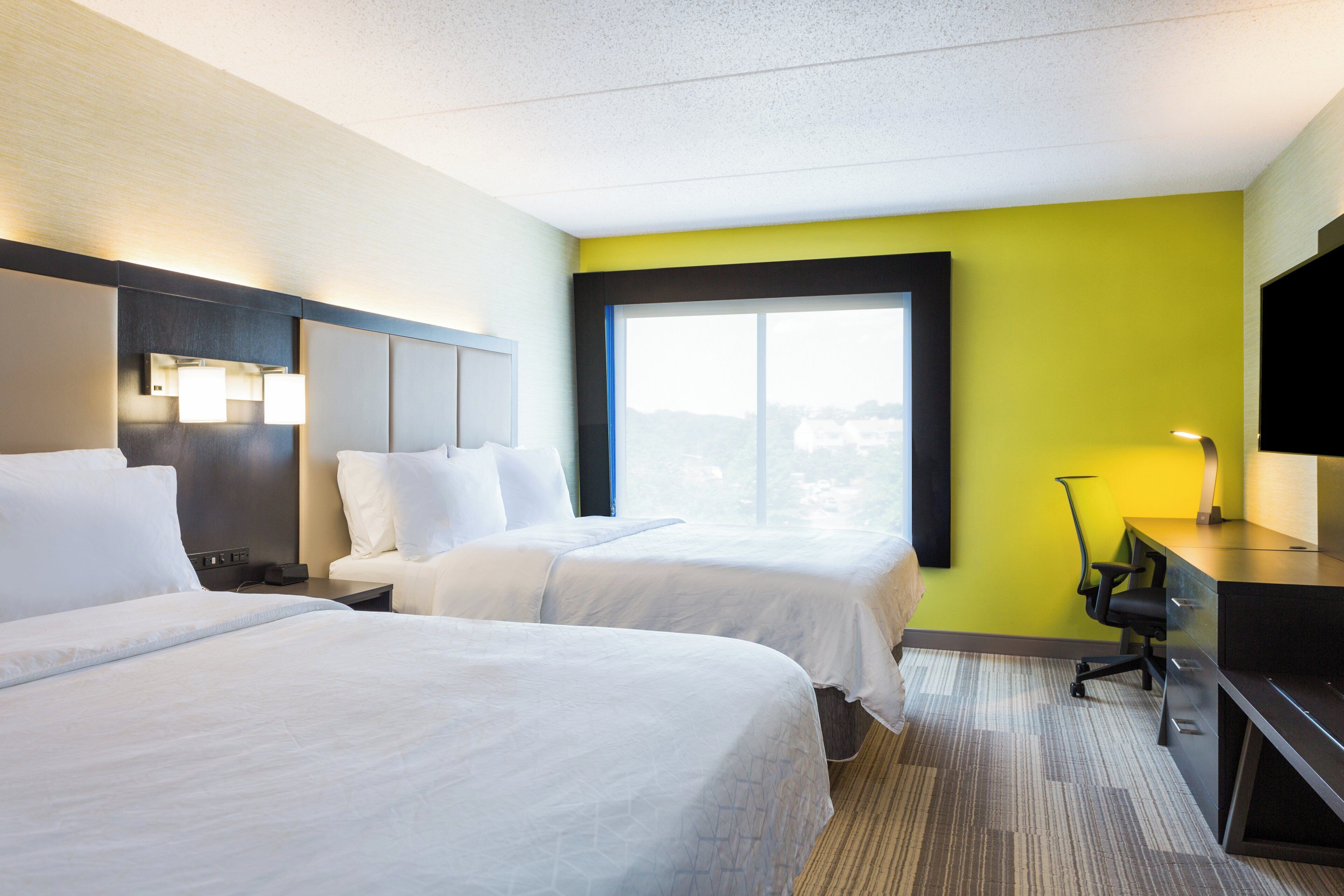 Een hotelkamer met twee bedden, een bureau, een stoel en een groot raam.