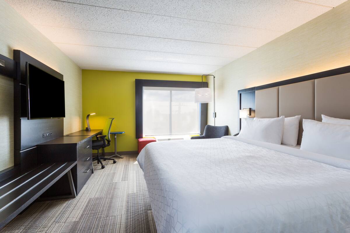 A hotel room with a bed, a desk, a chair, a TV, and a window.