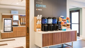 A coffee station with multiple coffee dispensers, a refrigerated display for yogurt, eggs, and milk, and a sign promoting coffee. - Holiday Inn Express Lorton by IHG (Lorton)