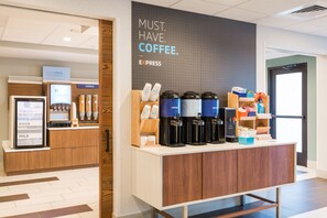En kaffestation med flere kaffemaskiner, et køleskab med yoghurt, æg og mælk, samt et skilt der reklamerer for kaffe.