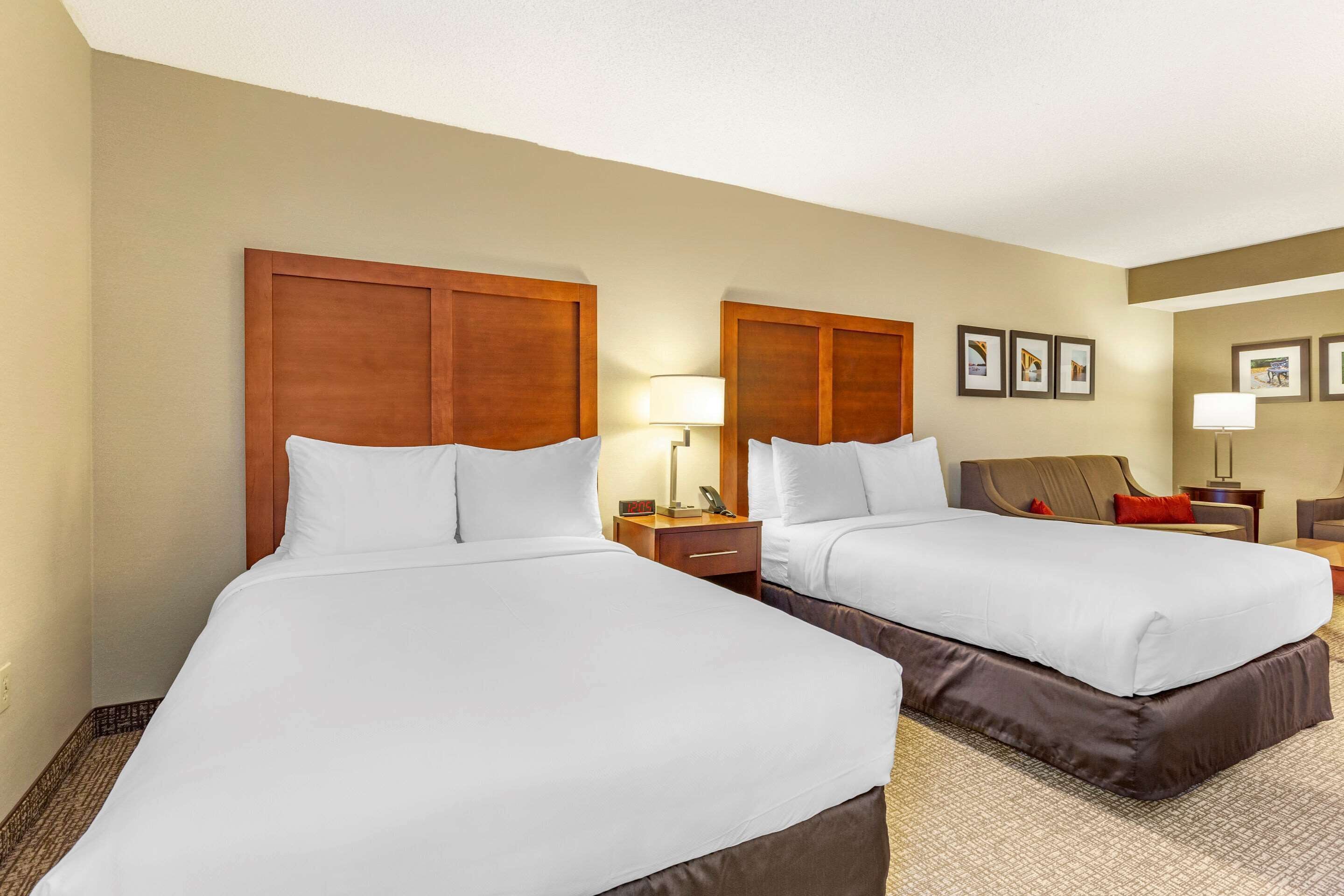 A hotel room with two beds, wooden headboards, a nightstand with a lamp, and framed pictures on the wall.