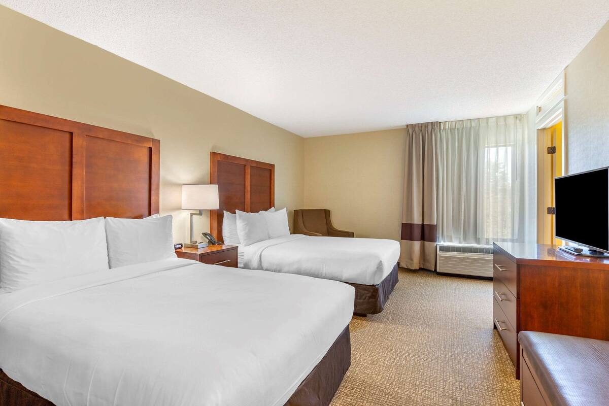 Quarto de hotel com duas camas, uma escrivaninha, televisão e janela com cortinas.