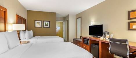 A hotel room with two beds, a desk with a computer, a television, and a small refrigerator.