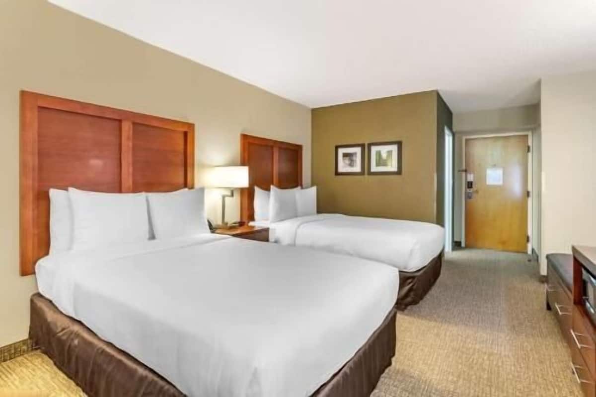 A hotel room with two beds, a wooden headboard, a lamp, and a door leading to another room.