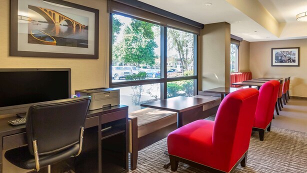 A hotel room with a desk, a chair, a television, a large window with a view of a bridge and trees, and a seating area with red chairs. - Comfort Inn Quantico (Stafford)