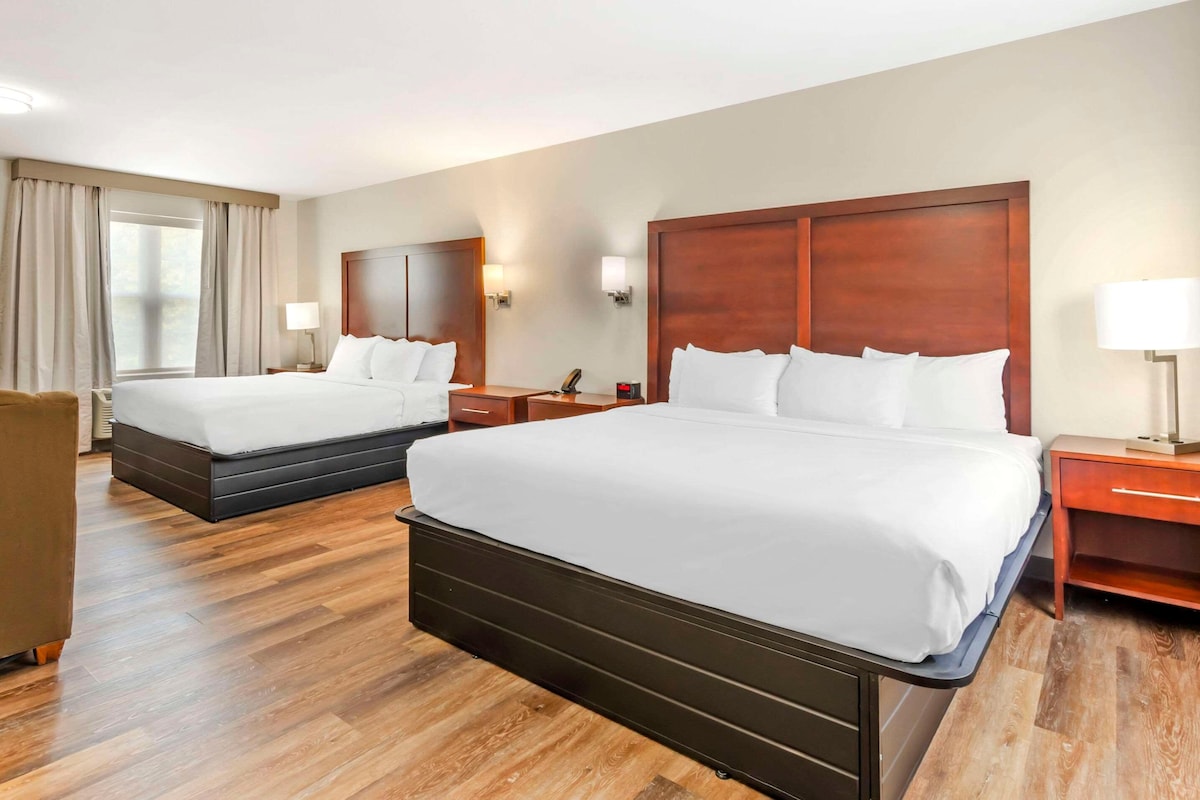 A hotel room with two beds, a wooden floor, a desk, and a chair.